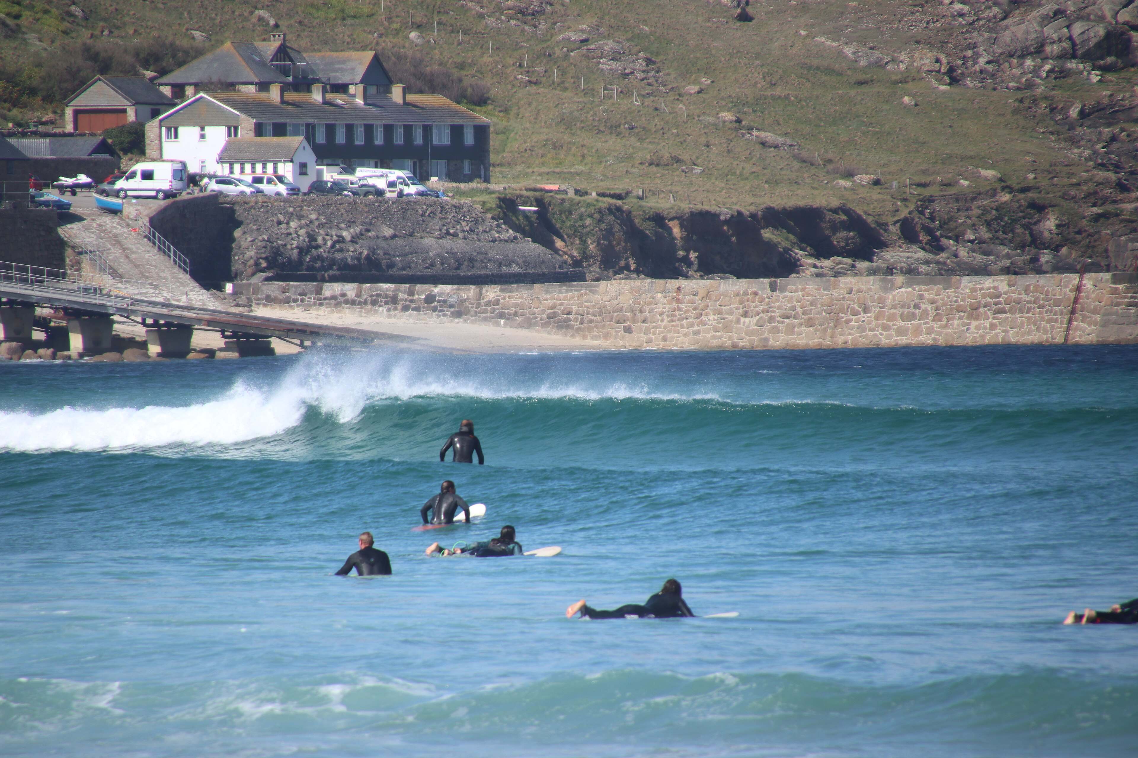 Surfers waiting in the line-up off a Cornish beach in low afternoon light — the climate the brands are built for.