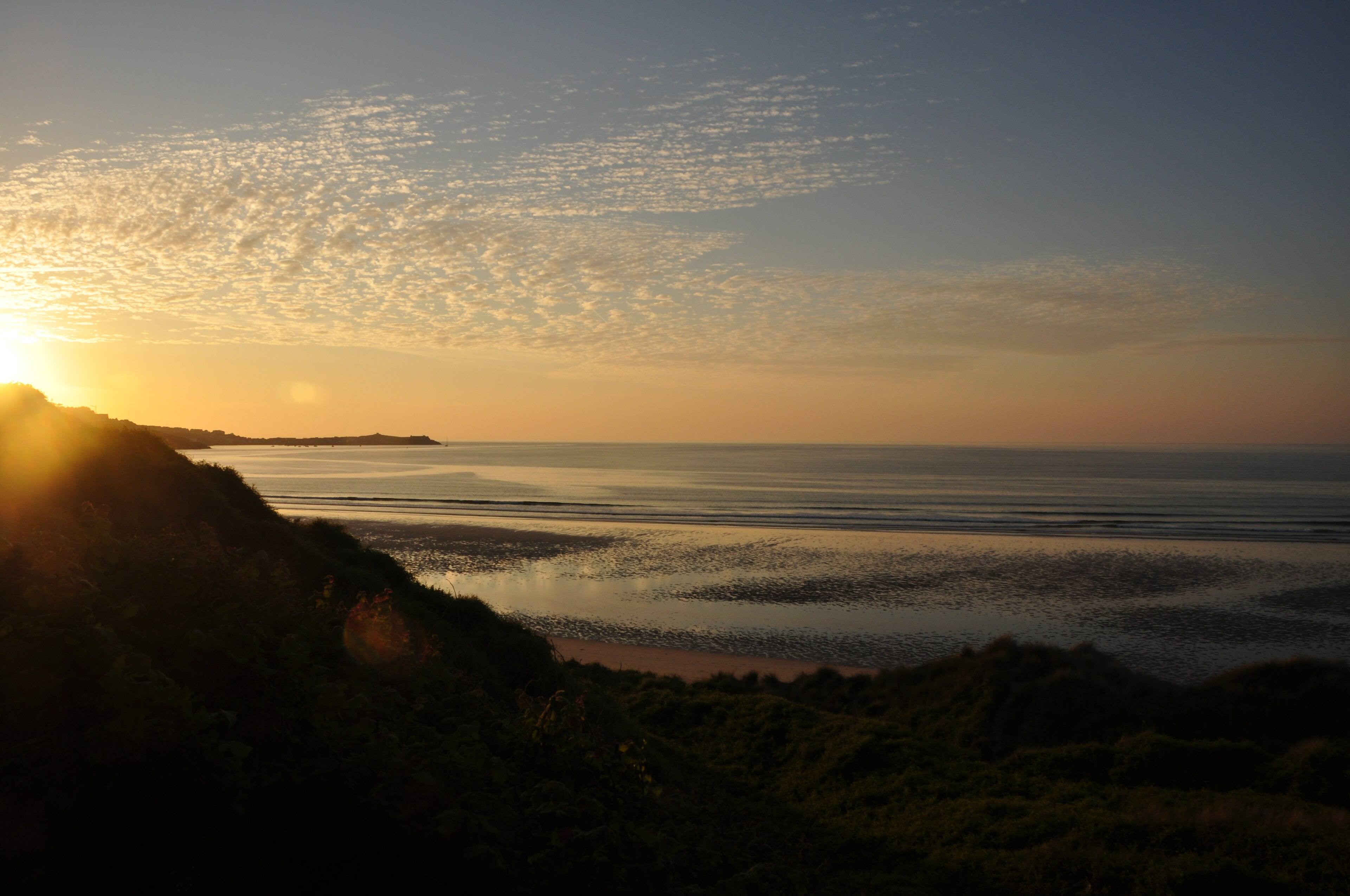 Evening light on the Cornish coast — golden hour turning the cliffs warm, the sea calm, and the sky soft pink.