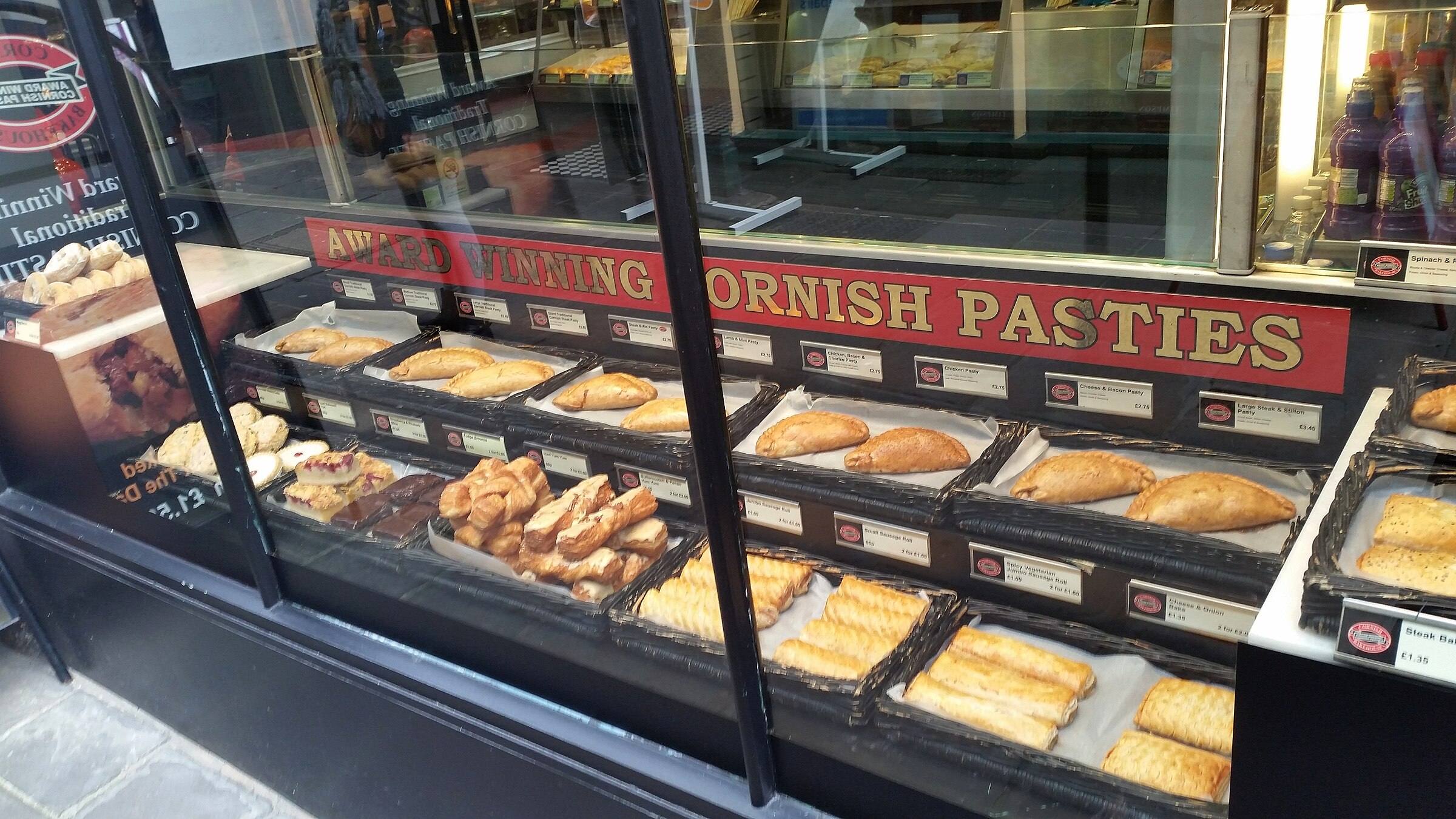 A traditional Cornish pasty, freshly baked with golden crimped pastry and steam rising from the cut end.