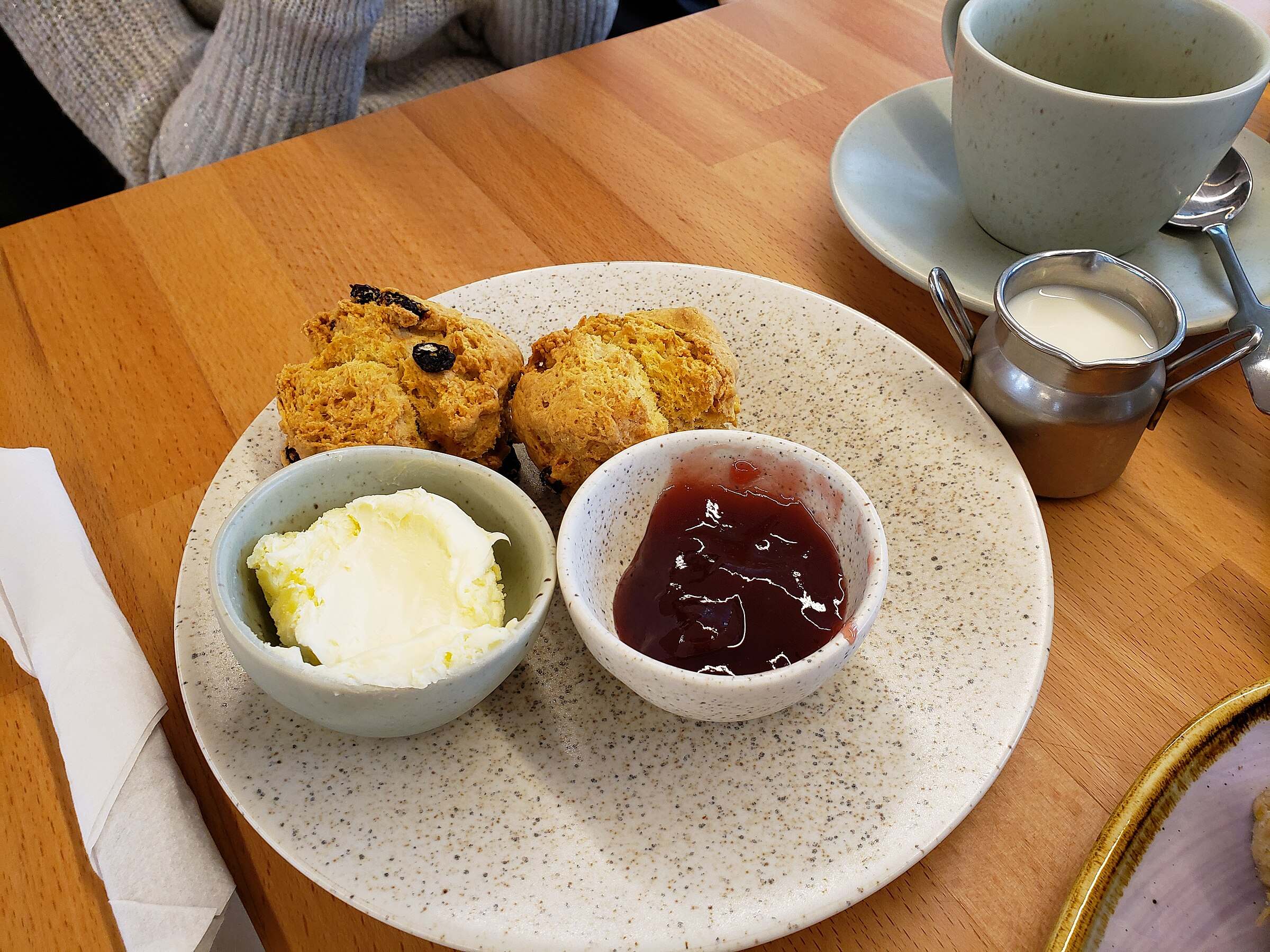 A traditional Cornish cream tea — scones, jam and Cornish clotted cream — laid out on a wooden table.