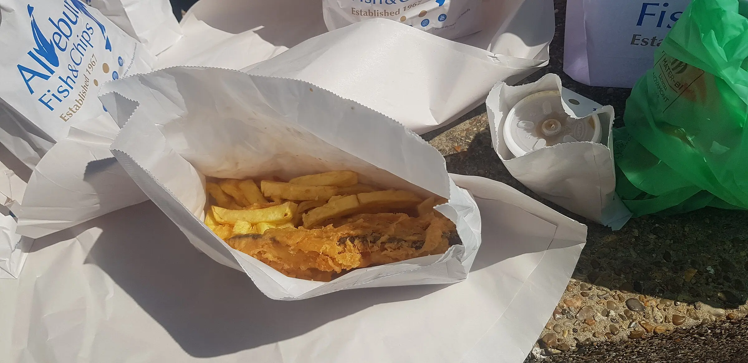 Fish and chips on the beach — golden battered fish with chips, eaten by the sea as they should be.