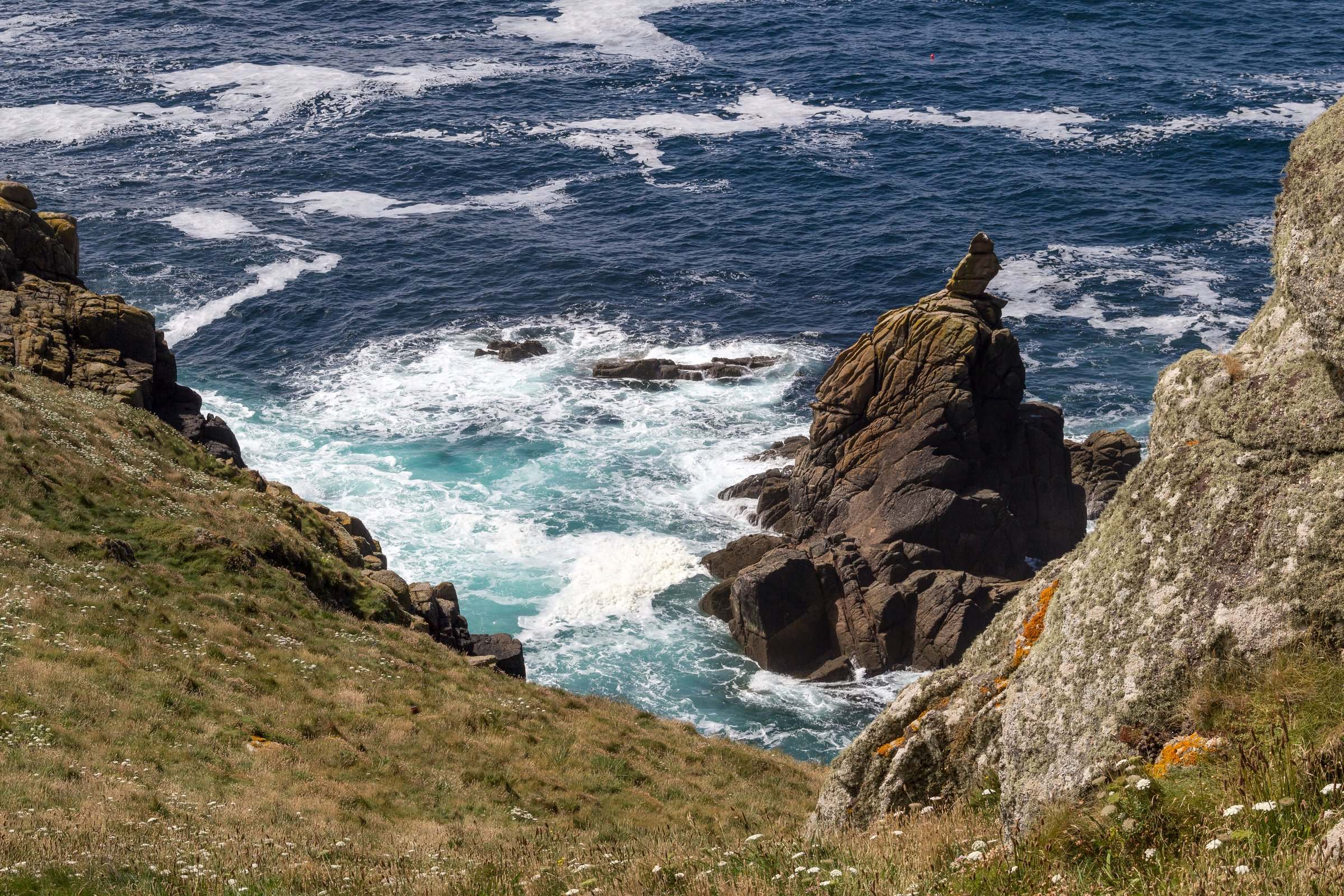 A grass coast-path stretch above granite cliffs and Atlantic surf on the south Cornwall coast.