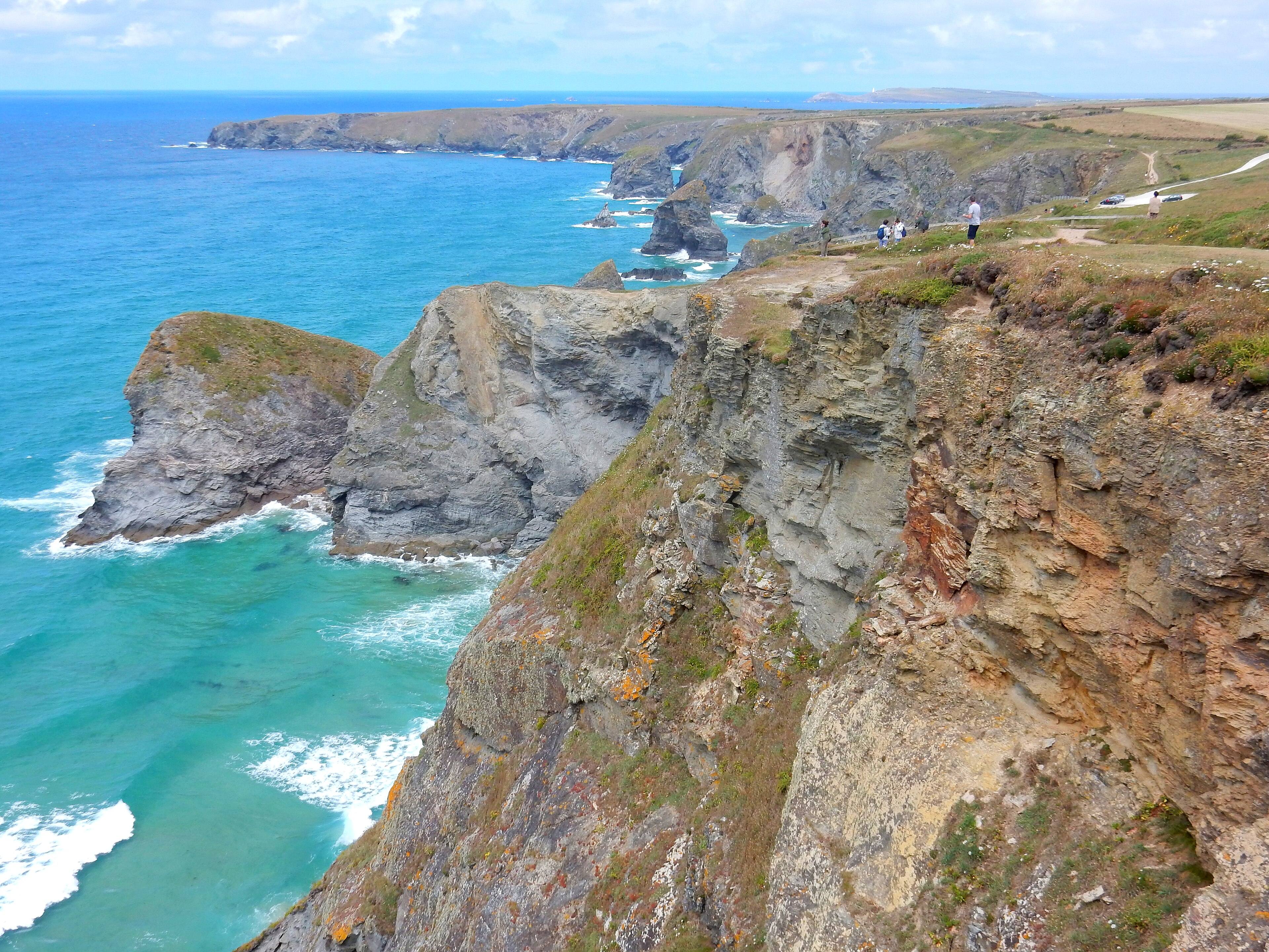 Bedruthan Steps on Cornwall's north coast — a row of granite sea-stacks rising from the Atlantic at low tide, with a long stretch of sand below the cliffs.