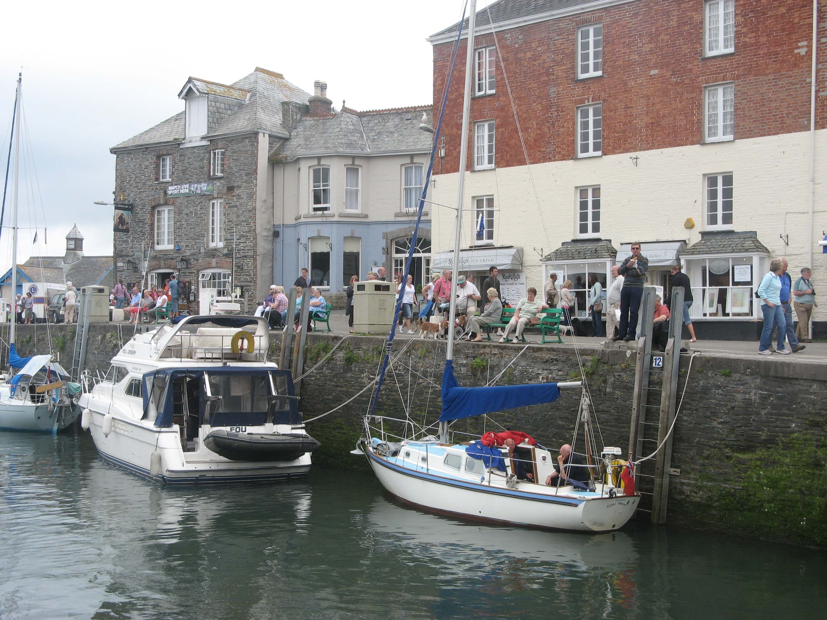 Padstow harbour at golden hour with fishing boats moored along the quay and the Camel estuary opening out behind.