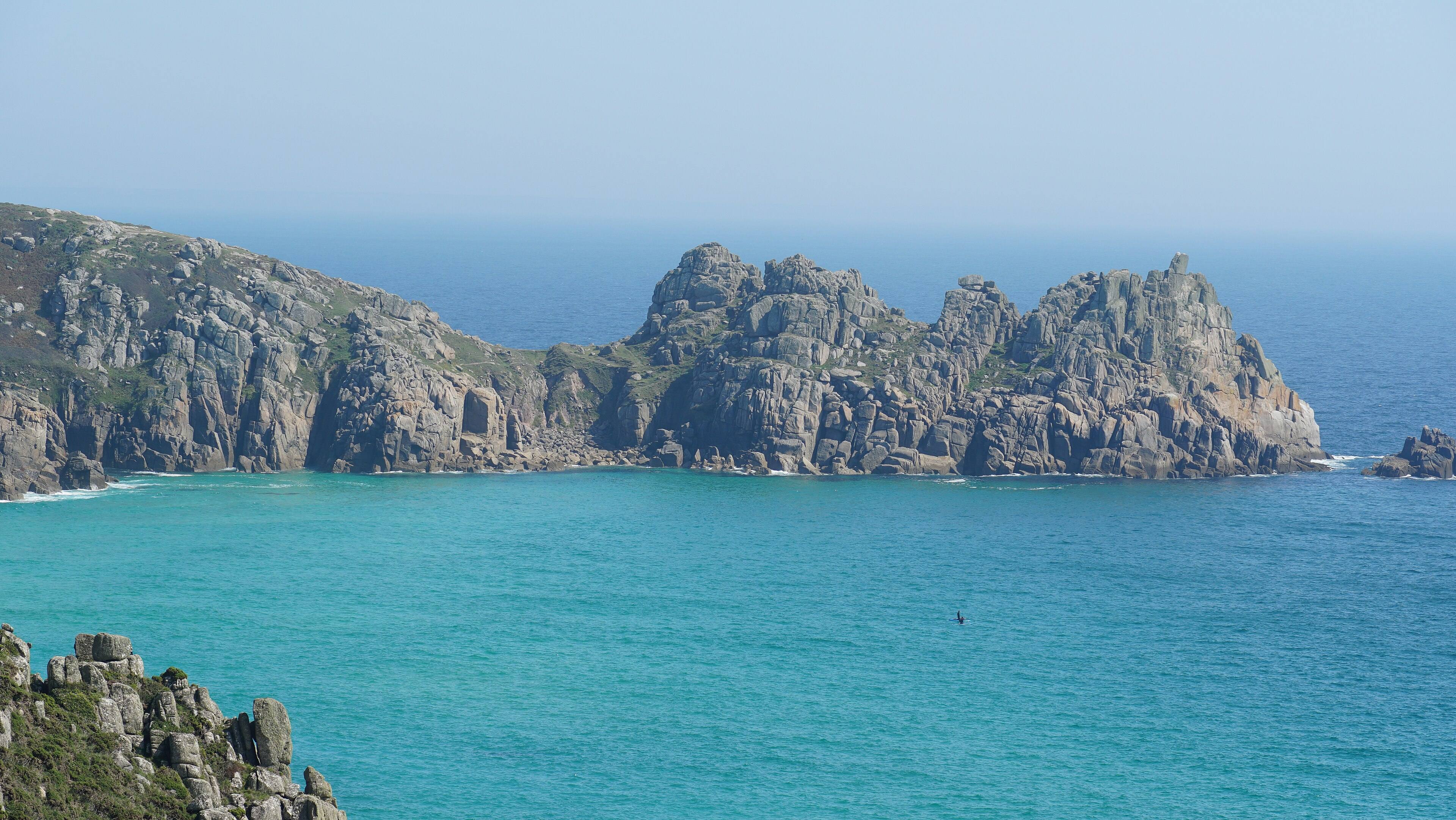 Porthcurno at low tide — turquoise water and white sand with the granite cliffs of the Minack Theatre above.