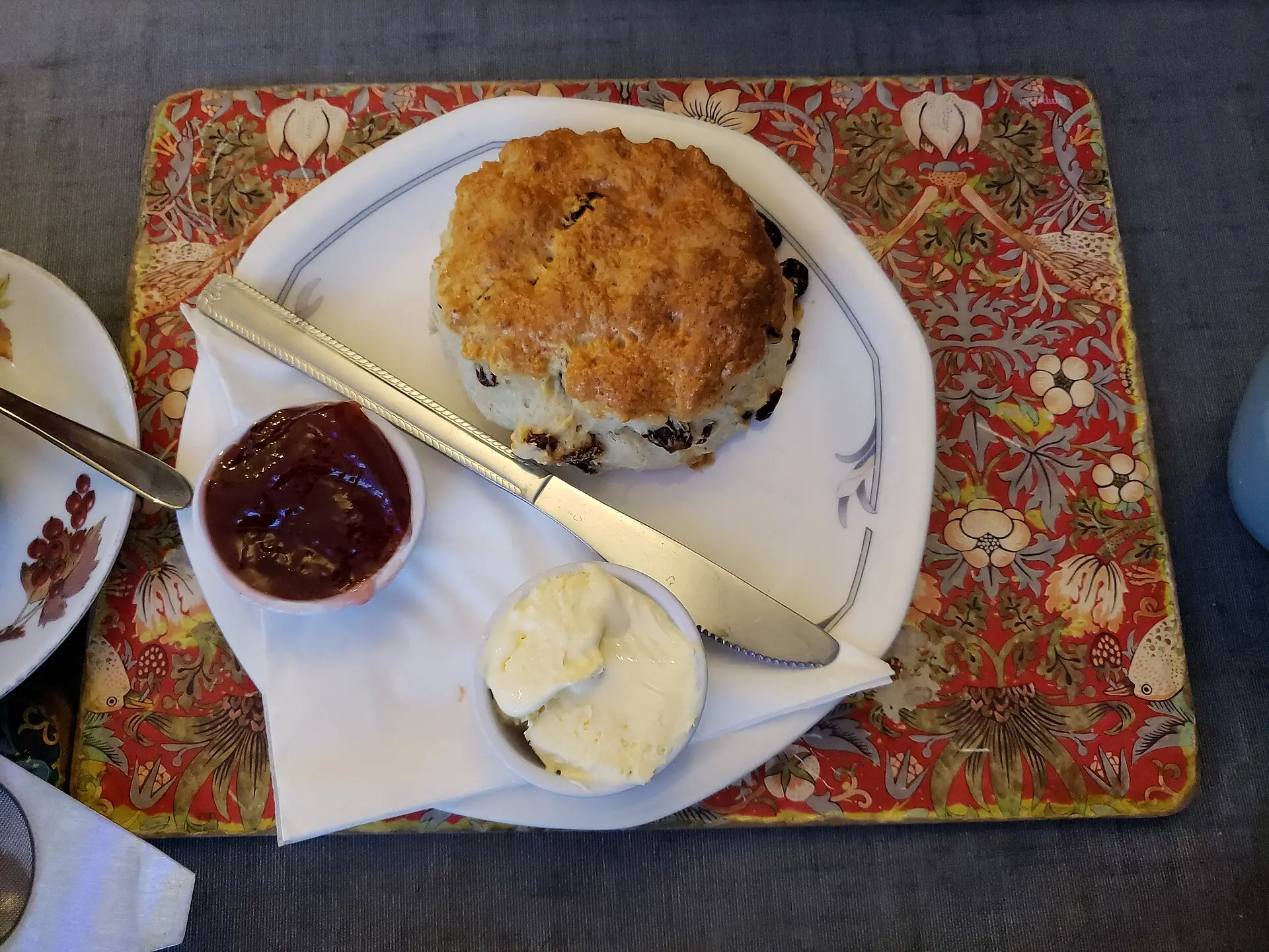 A Cornish cream tea — scones, clotted cream, and strawberry jam served on a white plate with a pot of tea.
