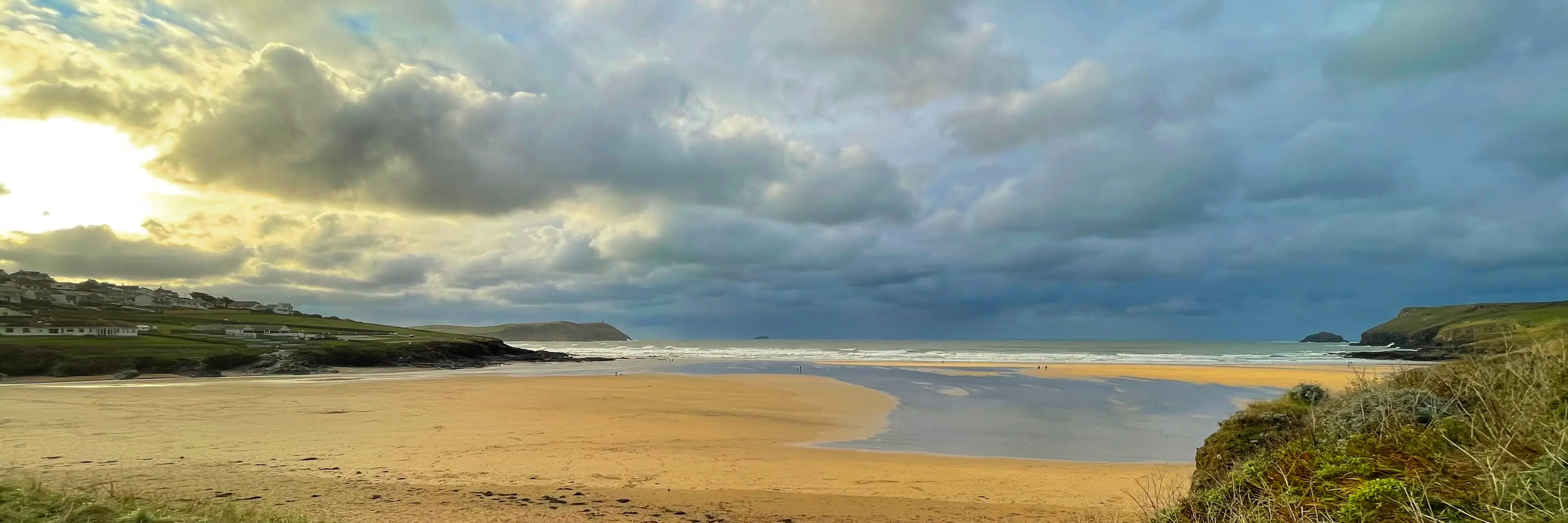 Polzeath beach at low tide — a wide expanse of sand with gentle surf, popular with families learning to surf.