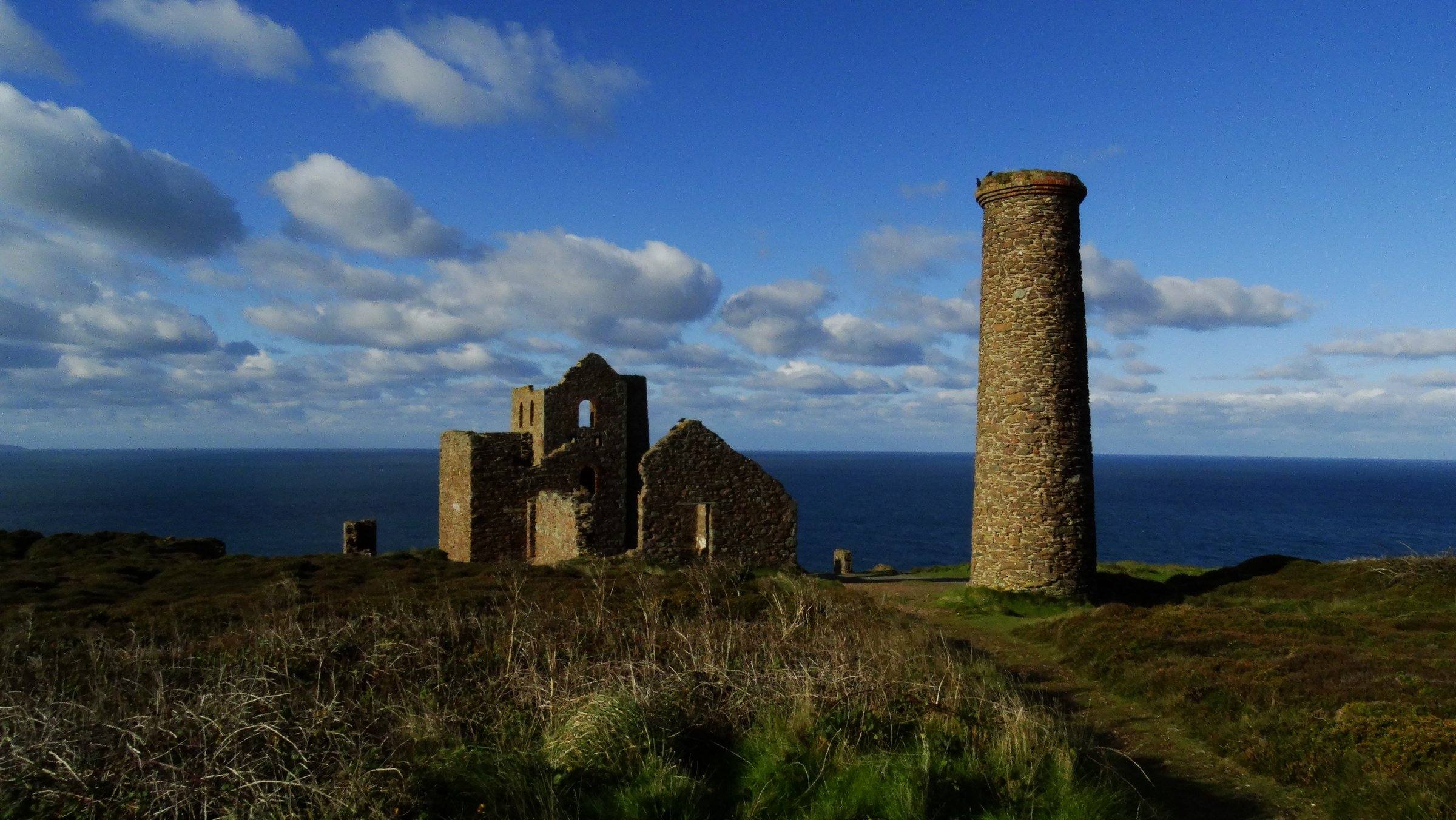 The South West Coast Path between St Agnes and Chapel Porth — heather on the headland and the Atlantic open to the west, with the silhouette of the old engine house at Wheal Coates above.